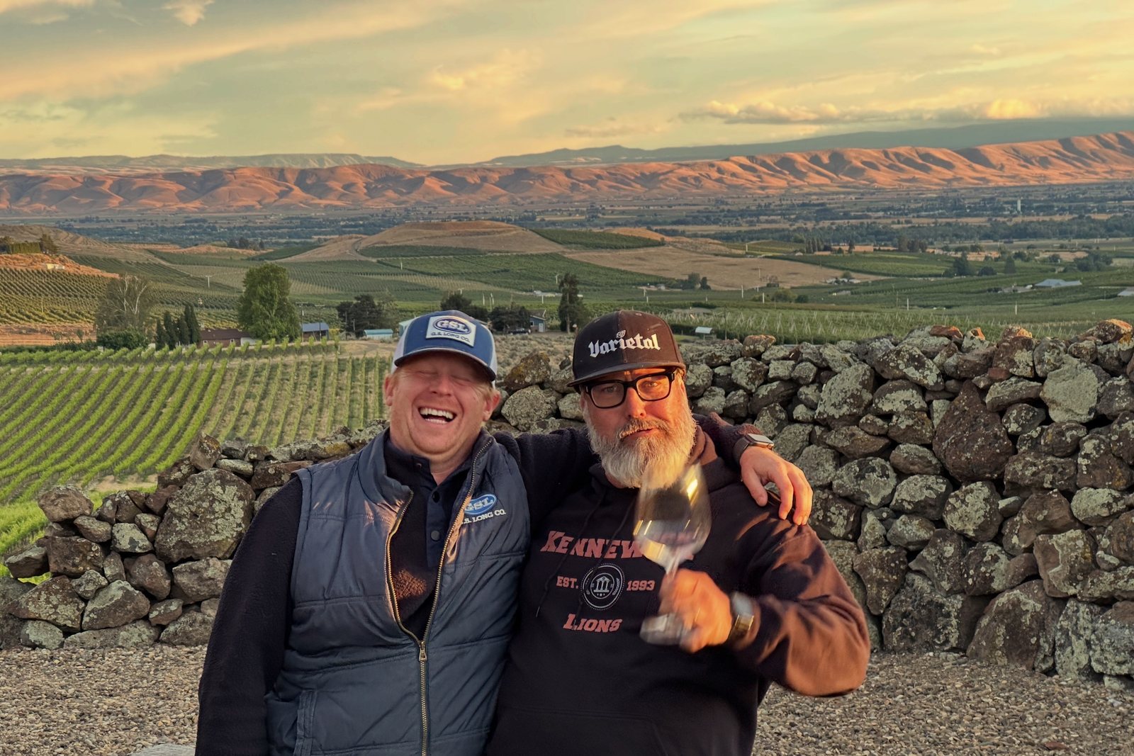 Two friends laughing with a glass of wine, the valley lit at sunset behind them