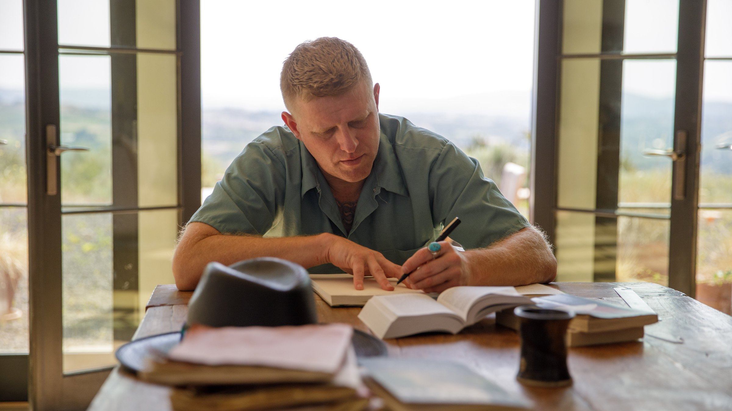 Andrew Schultz writing at the table, the valley through the glass doors