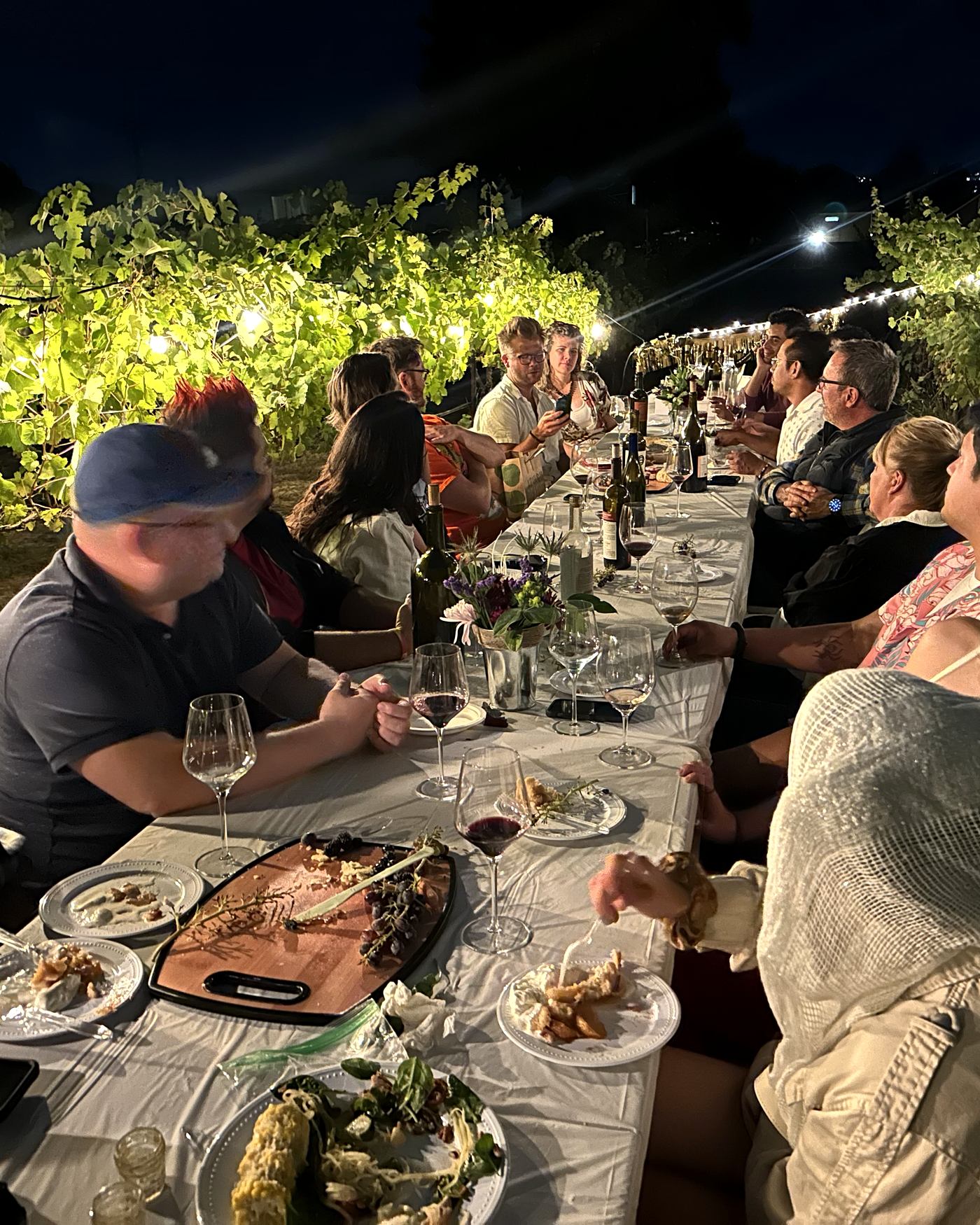 A long table set in the rows at night, full of guests, glasses and plates